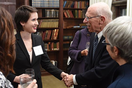 Photo of a female Chatham University student with a name tag and blazer, shaking the hand of a man in a suit at a networking event. 